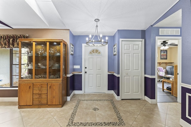 entrance foyer with ceiling fan with notable chandelier, visible vents, baseboards, and light tile patterned floors