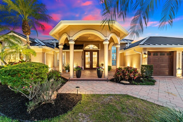 15730 Cedar Grove Ln, Wellington, FL 33414 - exterior entry at dusk featuring metal roof, an attached garage, a standing seam roof, stucco siding, and french doors