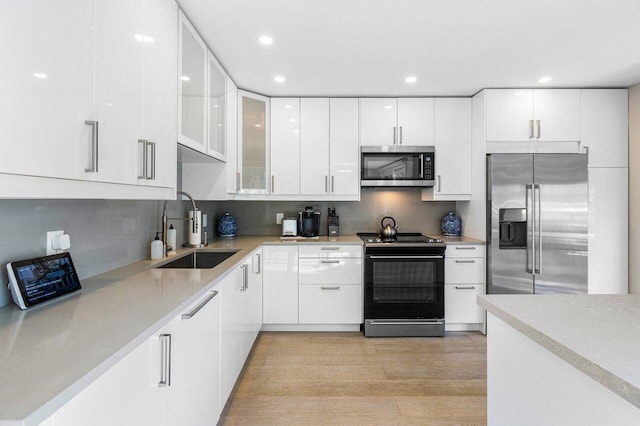 kitchen with white cabinets, stainless steel appliances, a sink, and light countertops