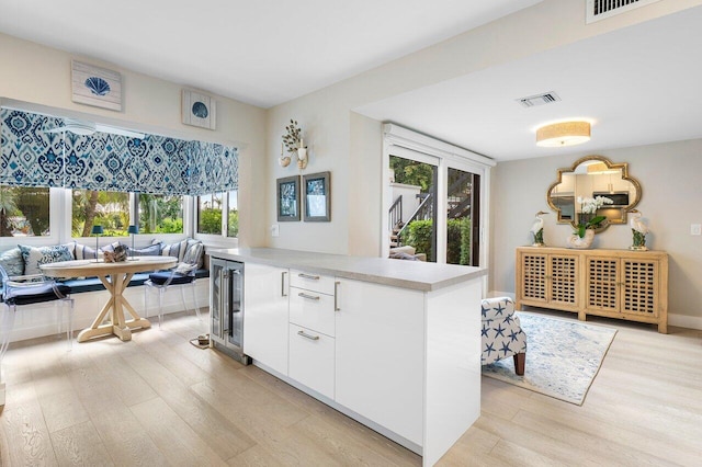 kitchen with beverage cooler, breakfast area, light countertops, light wood-type flooring, and white cabinetry