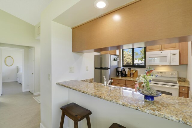 kitchen featuring a peninsula, white appliances, a sink, a kitchen breakfast bar, and light stone countertops