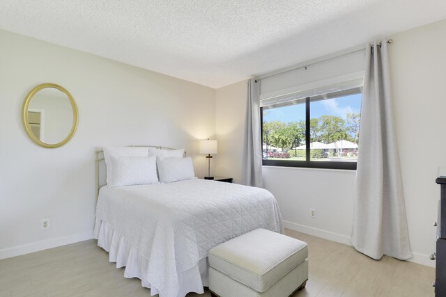 bedroom featuring light wood-style flooring, baseboards, and a textured ceiling