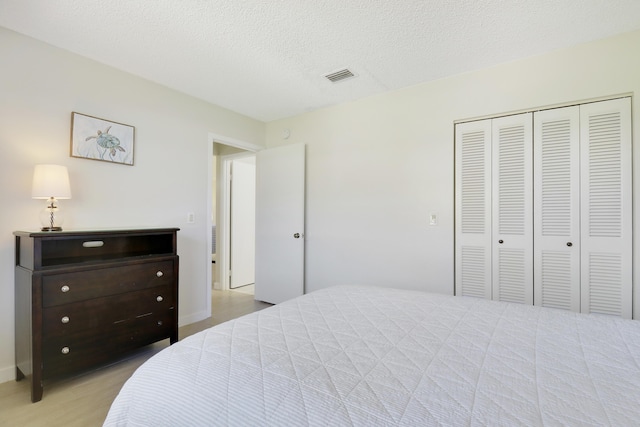 bedroom featuring a textured ceiling, wood finished floors, visible vents, baseboards, and a closet