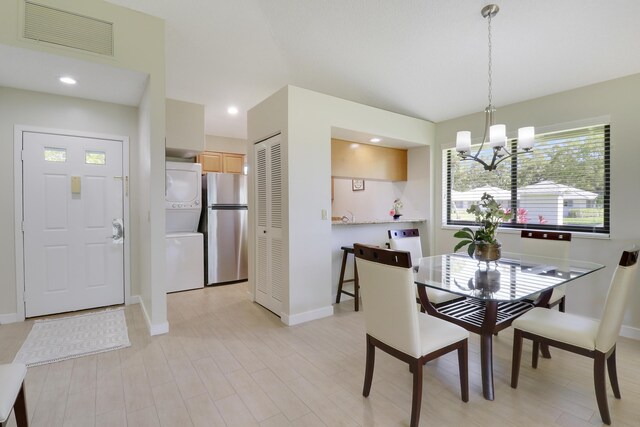 dining area featuring light wood finished floors, visible vents, stacked washer / dryer, and an inviting chandelier