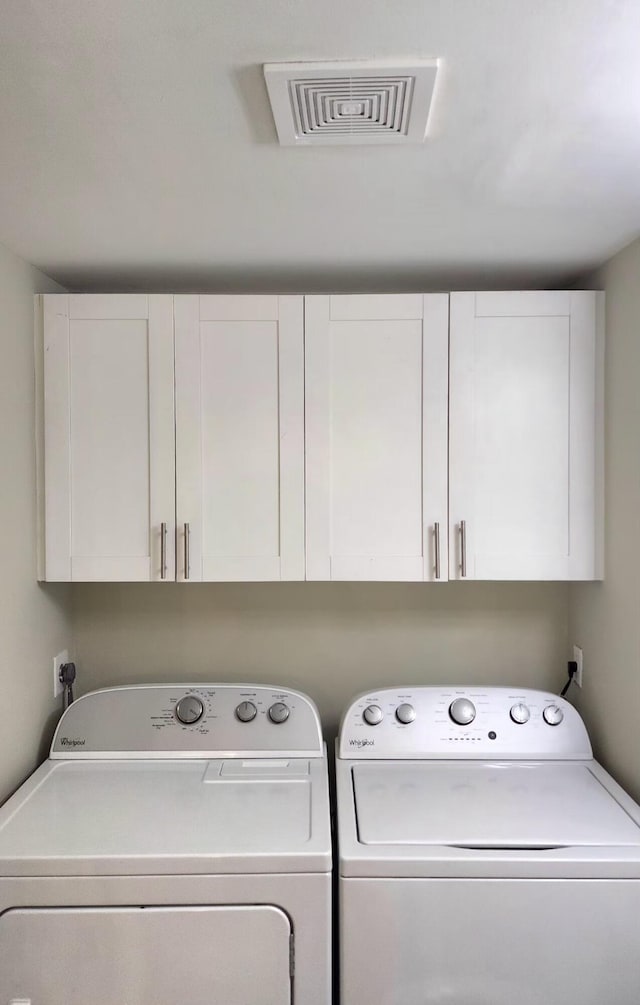 clothes washing area with washer and dryer, cabinet space, and visible vents