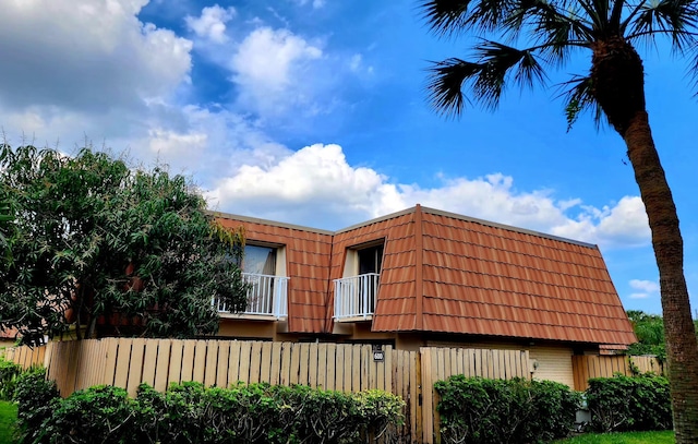 view of property exterior with fence, a tiled roof, a balcony, and mansard roof