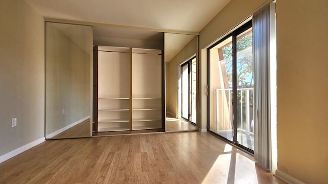 unfurnished bedroom with access to exterior, a closet, baseboards, and wood finished floors