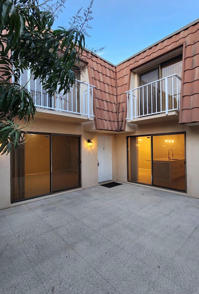 townhome / multi-family property featuring a tile roof, a patio, stucco siding, mansard roof, and a balcony