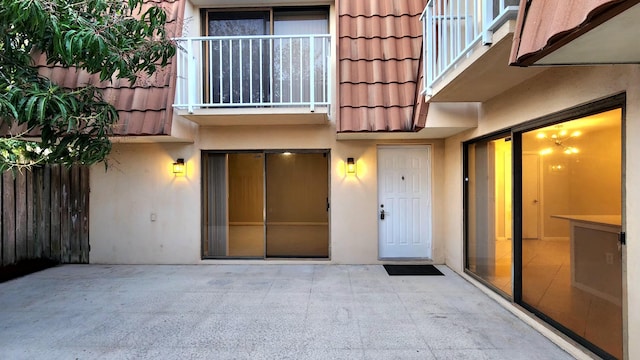 entrance to property featuring a patio, a tile roof, a balcony, and stucco siding