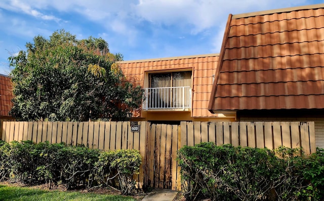 view of property exterior with a tiled roof, mansard roof, and fence