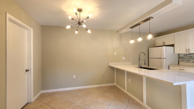 kitchen with light tile patterned floors, tasteful backsplash, freestanding refrigerator, a peninsula, and a sink