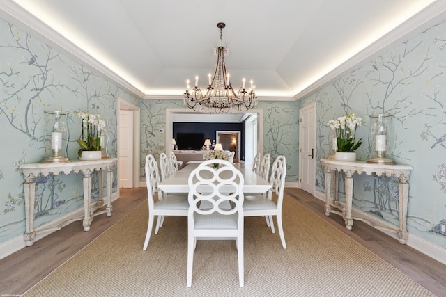 dining space with wallpapered walls, a raised ceiling, wood finished floors, and an inviting chandelier