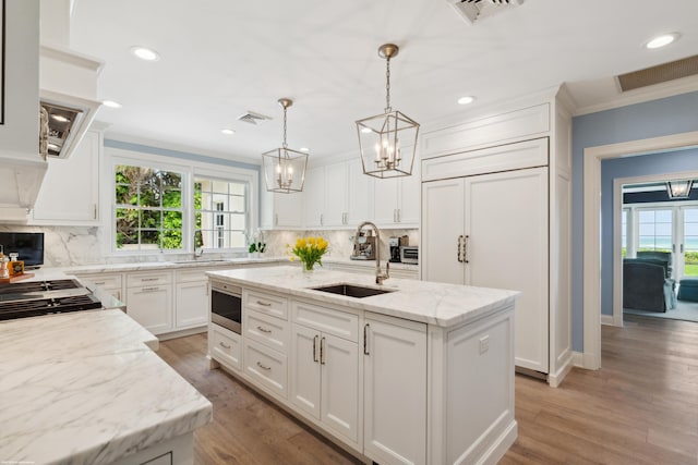 kitchen with a kitchen island with sink, built in appliances, a sink, and visible vents