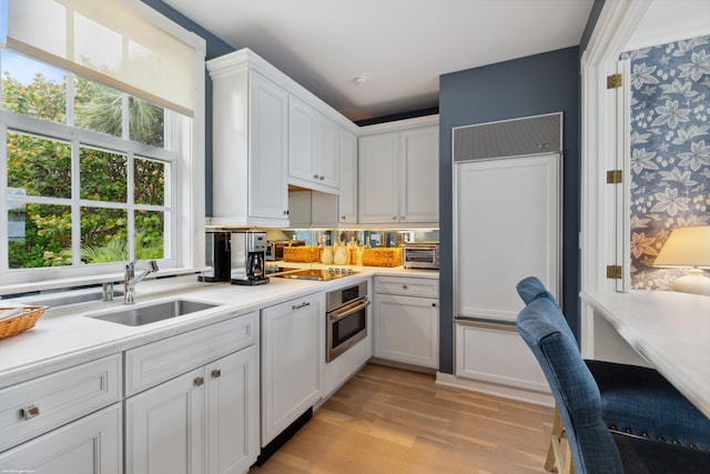 kitchen featuring light countertops, light wood-style floors, white cabinetry, stainless steel oven, and a sink