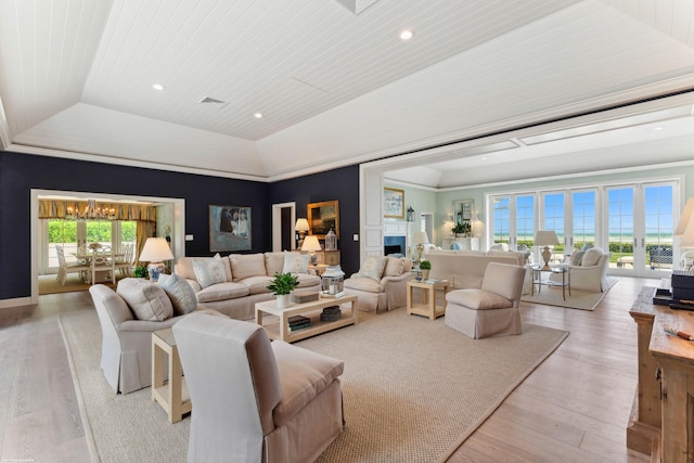 living area with a tray ceiling, light wood-type flooring, a fireplace, and visible vents