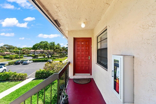 property entrance with a balcony, uncovered parking, and stucco siding