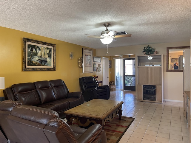 living room featuring visible vents, light tile patterned flooring, ceiling fan, a textured ceiling, and baseboards