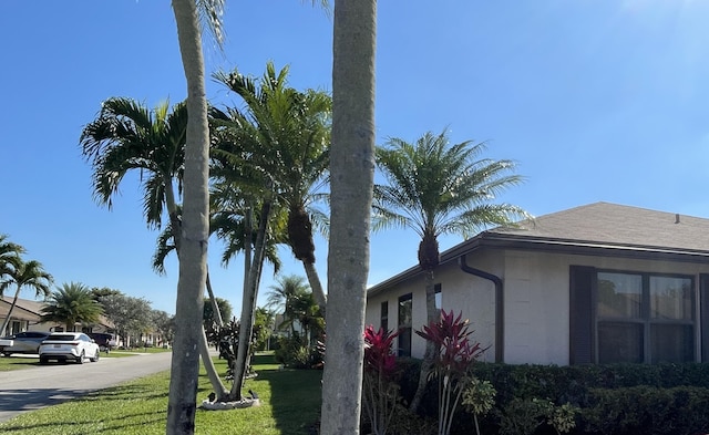 view of side of home with a yard, a shingled roof, and stucco siding