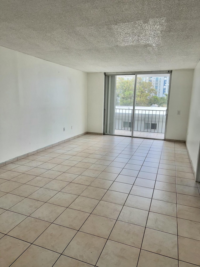 empty room with a wall of windows, a textured ceiling, baseboards, and light tile patterned floors