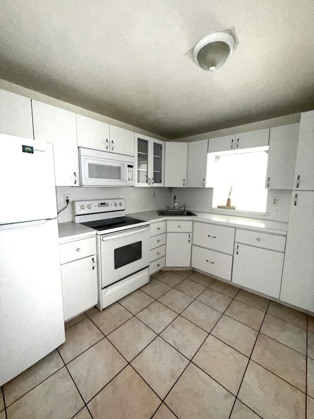 kitchen featuring light tile patterned floors, light countertops, white cabinetry, a sink, and white appliances