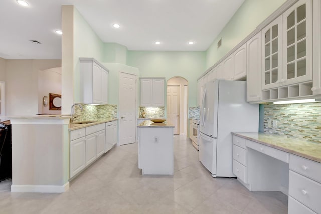 kitchen featuring arched walkways, white appliances, a sink, white cabinetry, and glass insert cabinets