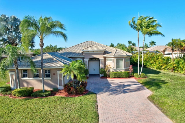 mediterranean / spanish-style house featuring decorative driveway, a tile roof, a front lawn, and stucco siding