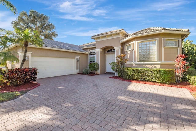 mediterranean / spanish house with decorative driveway, a tile roof, an attached garage, and stucco siding