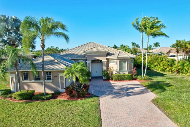 view of front of house featuring a tiled roof, a front lawn, decorative driveway, and stucco siding