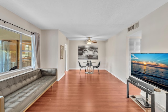 living room with visible vents, ceiling fan, baseboards, wood finished floors, and a textured ceiling