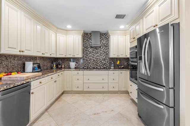 kitchen featuring visible vents, appliances with stainless steel finishes, cream cabinetry, wall chimney range hood, and backsplash