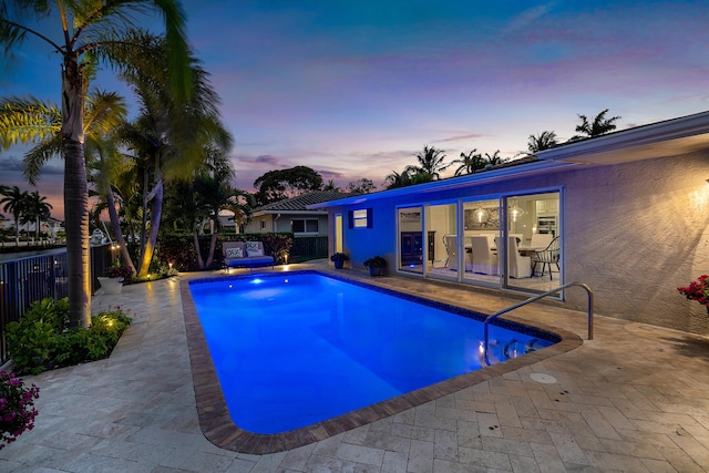 pool at dusk featuring a patio area, a fenced backyard, and a fenced in pool