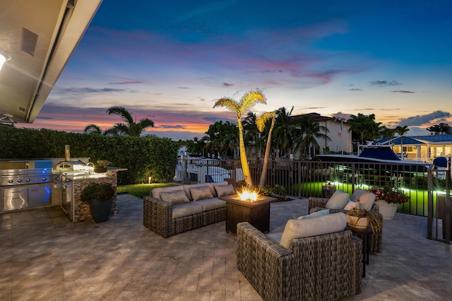 patio terrace at dusk with an outdoor living space with a fire pit, a grill, fence, and area for grilling