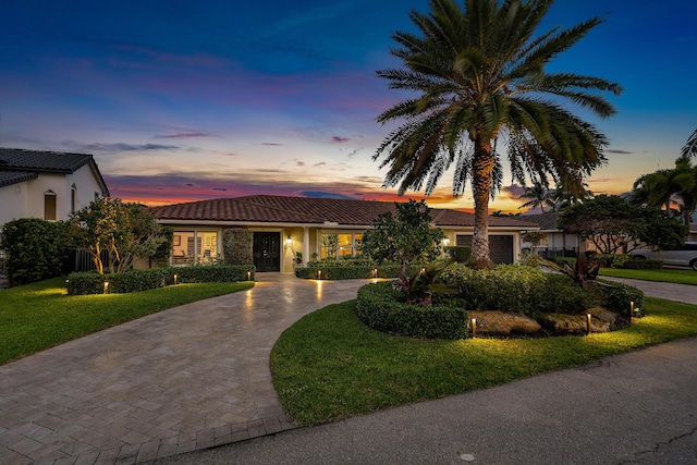 view of front facade featuring decorative driveway, stucco siding, a garage, a tiled roof, and a front lawn