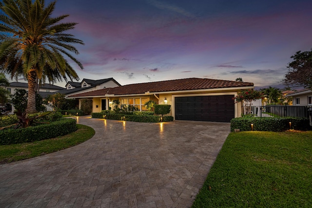 view of front of property with a garage, a tile roof, decorative driveway, a lawn, and stucco siding