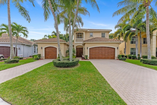 mediterranean / spanish-style home featuring a front yard, stucco siding, a garage, a tiled roof, and decorative driveway