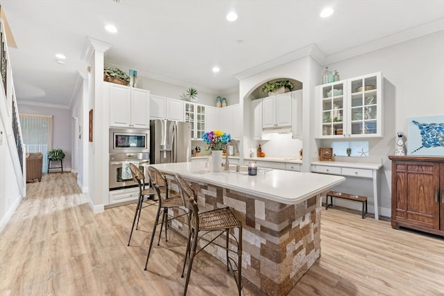 kitchen with glass insert cabinets, crown molding, light wood-type flooring, appliances with stainless steel finishes, and a kitchen breakfast bar