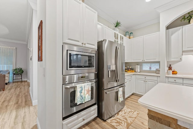 kitchen featuring light wood finished floors, crown molding, light countertops, appliances with stainless steel finishes, and white cabinetry