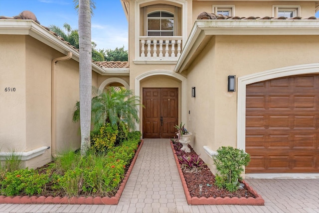 doorway to property featuring a garage, a balcony, a tile roof, and stucco siding