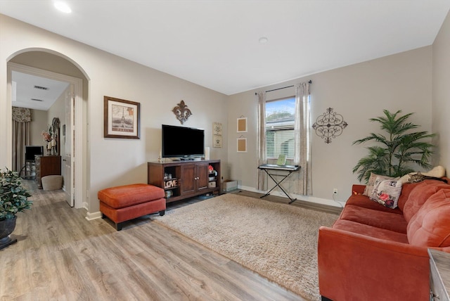 living room with light wood-type flooring, arched walkways, and baseboards