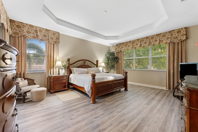 bedroom with a tray ceiling, multiple windows, baseboards, and light wood-style flooring