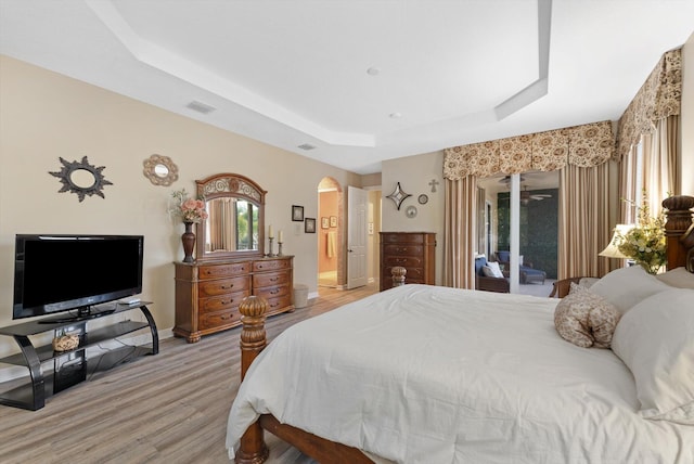 bedroom featuring visible vents, a tray ceiling, light wood-style flooring, arched walkways, and access to outside