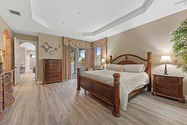 bedroom with visible vents, access to outside, arched walkways, light wood finished floors, and a raised ceiling