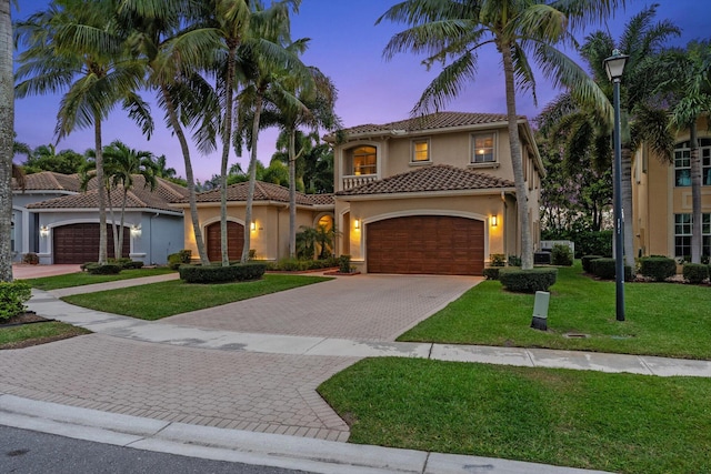 mediterranean / spanish-style house featuring stucco siding, driveway, a tile roof, a yard, and an attached garage