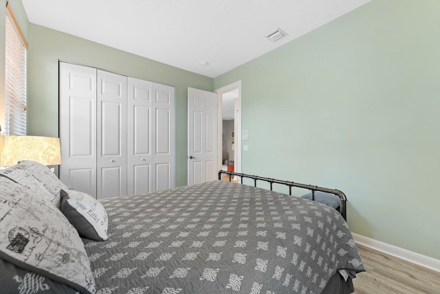 bedroom featuring wood finished floors, visible vents, a closet, and baseboards