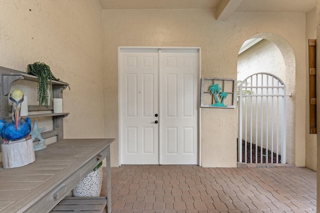 interior space featuring beam ceiling, a textured wall, and arched walkways