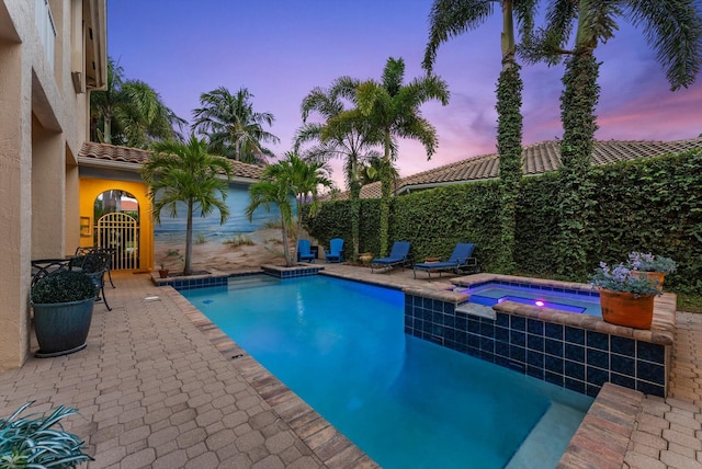 pool at dusk featuring a fenced in pool, an in ground hot tub, a fenced backyard, and a patio area