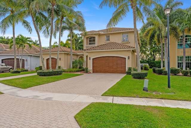mediterranean / spanish house with a tiled roof, a front yard, stucco siding, decorative driveway, and an attached garage