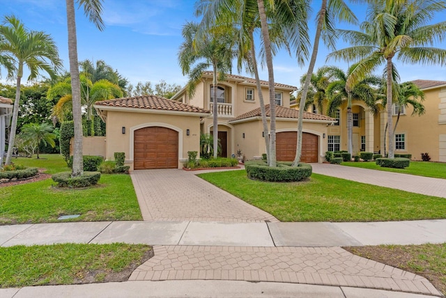 mediterranean / spanish-style house with a front yard, stucco siding, a garage, a tile roof, and decorative driveway