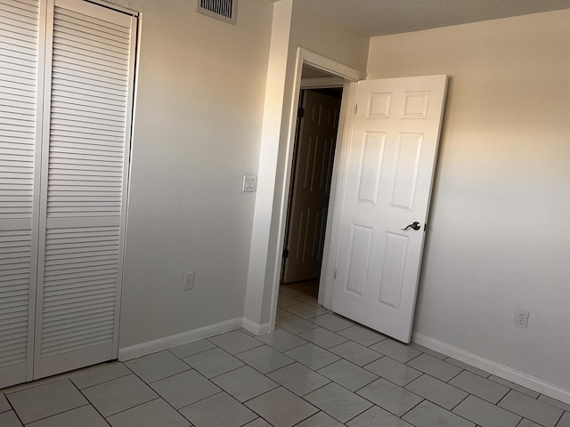 unfurnished bedroom featuring light tile patterned floors, baseboards, visible vents, and a closet