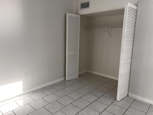 unfurnished bedroom featuring light tile patterned floors, a closet, visible vents, and baseboards